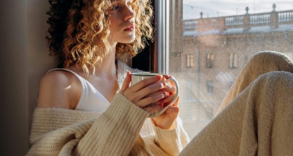 Frau im Funktionsmodus blickt nachdenklich aus dem Fenster – Thema Nervensystem und Erschöpfung